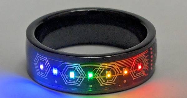 Black tungsten ring with seven rainbow LEDs lit, casting a rainbow glow